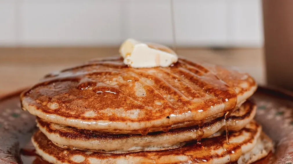 Pila de hotcakes con un cuadro de mantequilla y miel escurriendo, en plato de barro