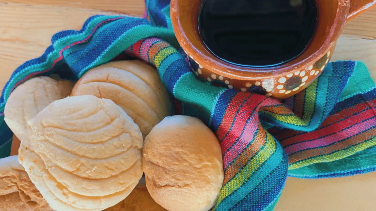 Pan de bacurimi sobre una servilleta de colores junto a un jarrito de barro con café de olla