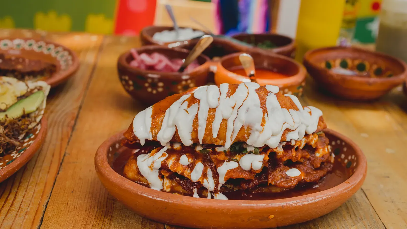 Torta ahogada de borrego bañada en consomé picante y crema, servida en plato de barro sobre mesa de madera