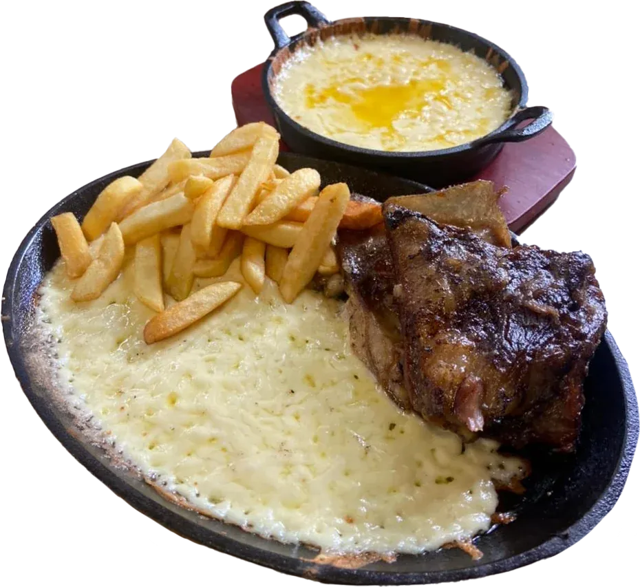 Costilla especial de borrego asada con queso fundido gratinado y papas fritas en plancha de hierro, junto a una cazuelita de queso fundido